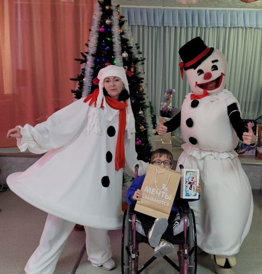 двое костюмированных взрослых поздравляют мальчика на инвалидном кресле